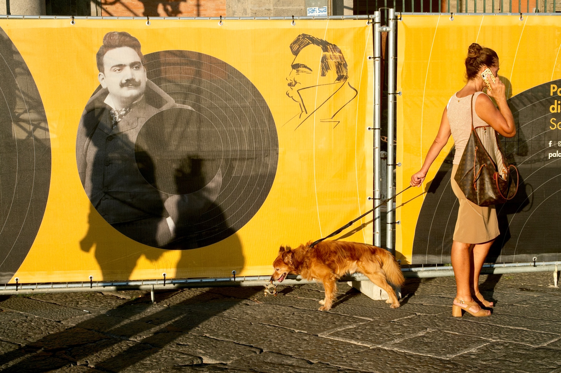 Woman walking a dog past a Caruso poster, Naples